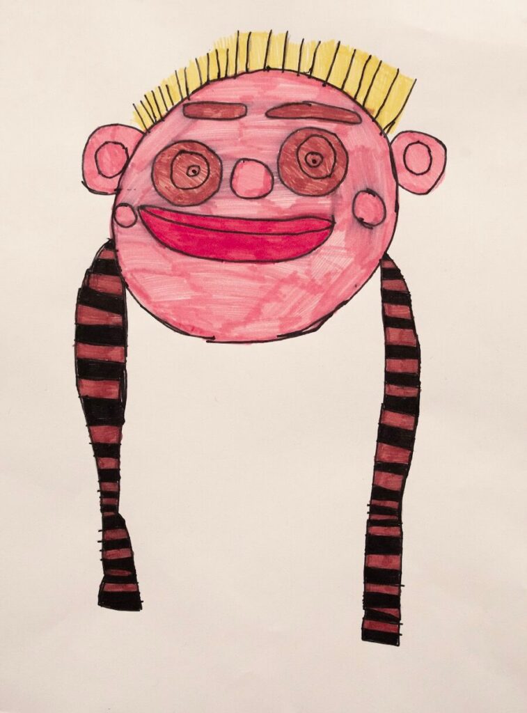 A smiling pink face with yellow spikey hair on the top of the head and brown stripy braids at the bottom.